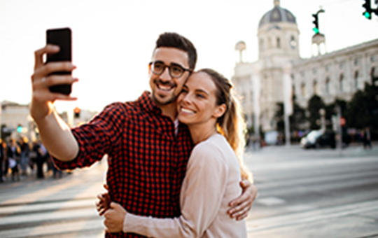 Young couple taking a selfie in front of a landmark while out-of-province for a weekend getaway