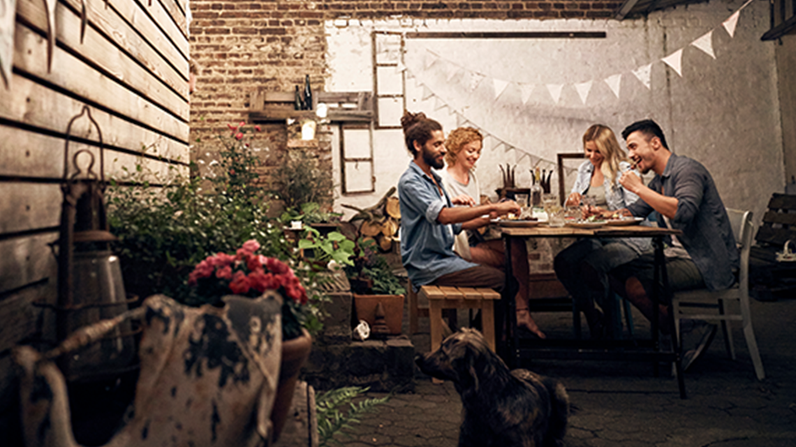 Four people sitting at a table, dinning al fresco in an urban backyard